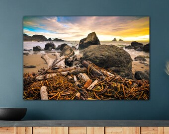 May include: A photograph of a rocky beach with driftwood and seaweed. The sky is a vibrant orange and pink, with clouds. The photo is framed and hanging on a wall above a wooden cabinet.