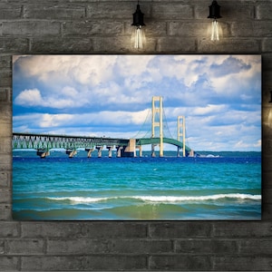 May include: A photograph of the Mackinac Bridge in Michigan. The bridge is a suspension bridge with a green and white color scheme. The bridge spans a body of water with blue water and white waves. The sky is blue with white clouds.