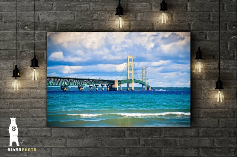 May include: A photograph of the Mackinac Bridge in Michigan. The bridge is a suspension bridge with a green and white color scheme. The bridge spans a body of water with blue water and white waves. The sky is blue with white clouds.