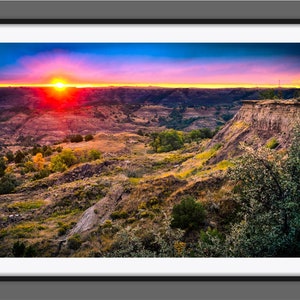 May include: A vibrant sunset over a rugged landscape with a deep canyon and rolling hills. The sky is a mix of pink, orange, and blue, with the sun setting in the distance.
