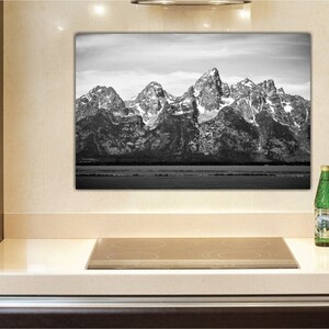 May include: Black and white photograph of a mountain range with snow-capped peaks. The photo is framed and hanging on a wall in a kitchen.