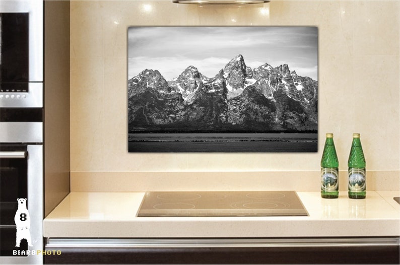 May include: Black and white photograph of a mountain range with snow-capped peaks. The photo is framed and hanging on a wall in a kitchen.