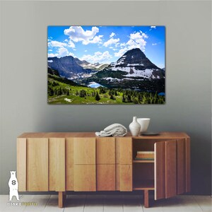 May include: A scenic landscape photograph featuring a mountain range with snow-capped peaks and a lake in the foreground. The sky is blue with white clouds.