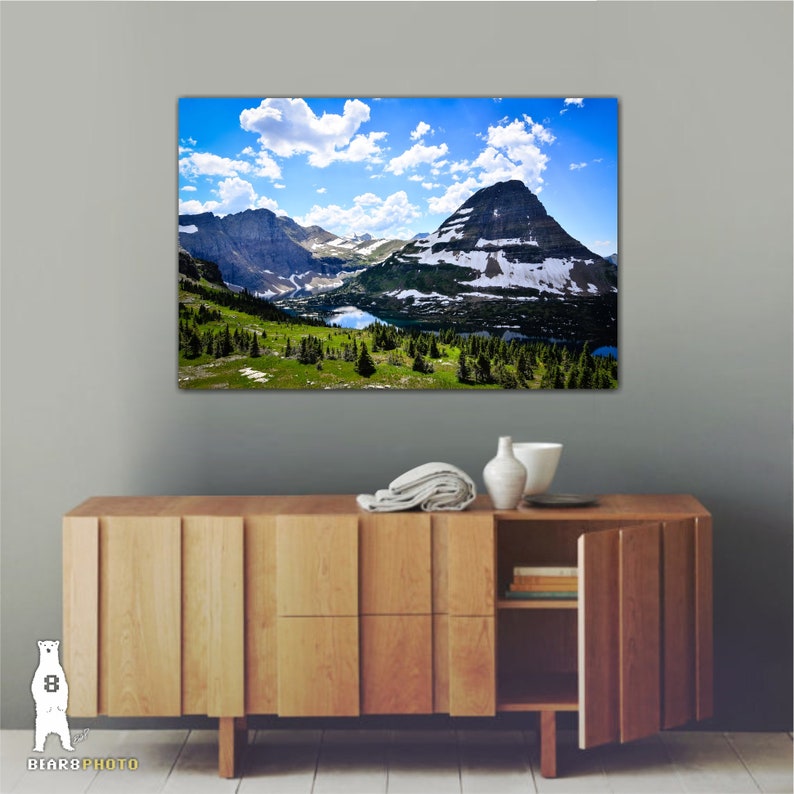 May include: A scenic landscape photograph featuring a mountain range with snow-capped peaks and a lake in the foreground. The sky is blue with white clouds.