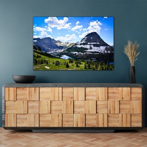 May include: A framed photograph of a mountain range with a lake in the foreground. The sky is blue with white clouds. The mountains are green and brown with snow on the peaks.
