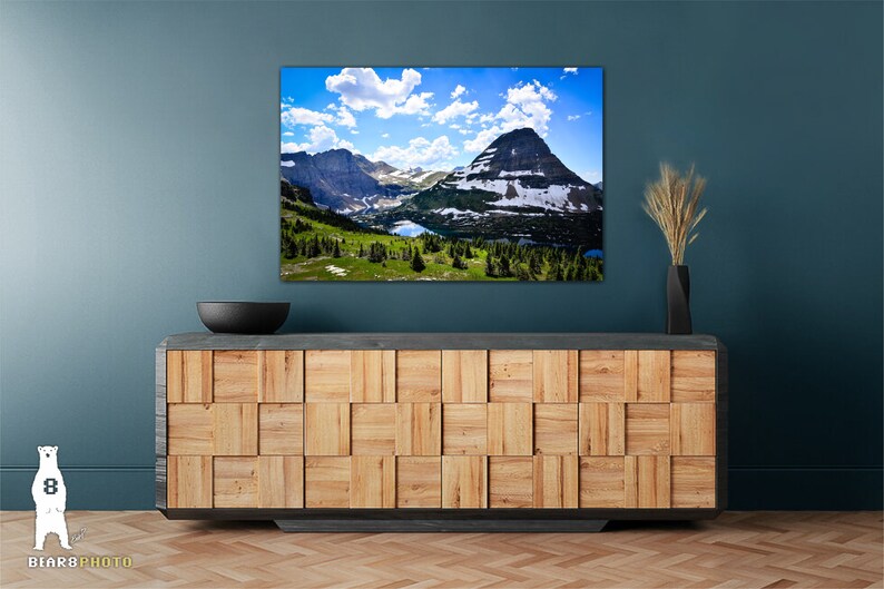 May include: A framed photograph of a mountain range with a lake in the foreground. The sky is blue with white clouds. The mountains are green and brown with snow on the peaks.