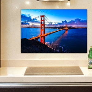 May include: A photograph of the Golden Gate Bridge in San Francisco, California. The bridge is lit up at night, and the water is dark blue. The sky is a deep blue with clouds.