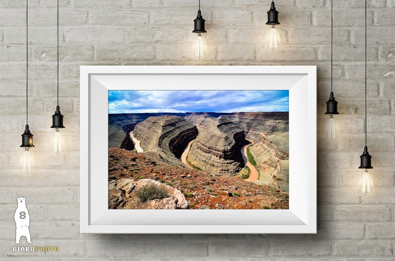 May include: A panoramic view of a winding river cutting through a canyon with layered rock formations. The sky is blue with white clouds.