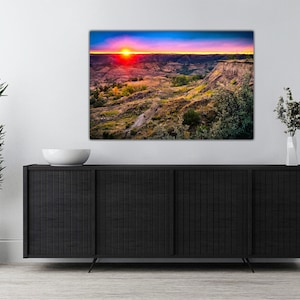 May include: A colorful sunset over a canyon landscape with a vibrant red sky and a bright orange sun. The canyon is covered in green vegetation and brown rock formations.