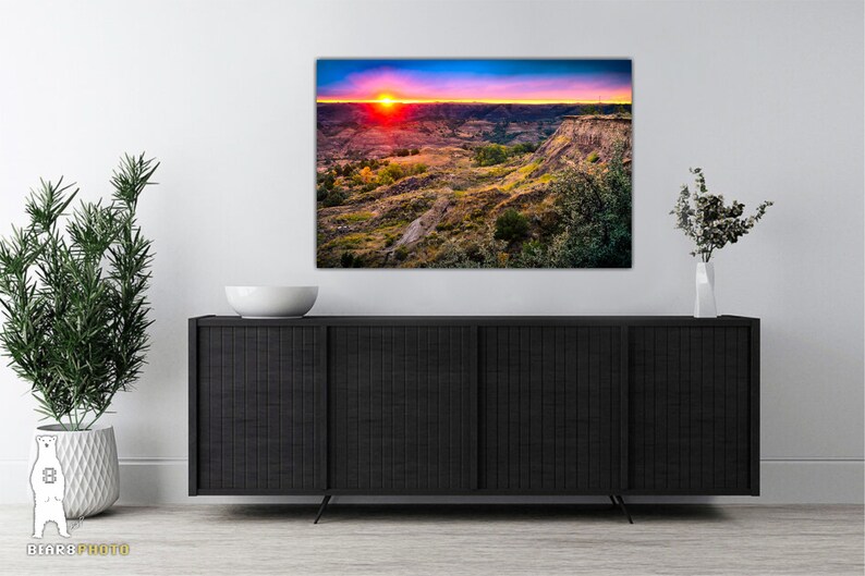 May include: A colorful sunset over a canyon landscape with a vibrant red sky and a bright orange sun. The canyon is covered in green vegetation and brown rock formations.