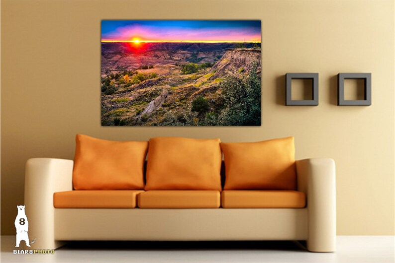 May include: A panoramic photograph of a canyon landscape with a vibrant sunset in the background. The sky is a mix of pink, orange, and blue hues, with the sun setting behind the canyon walls. The canyon is a rugged and rocky landscape, with a variety of vegetation growing on the slopes.