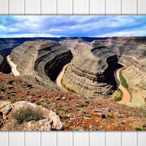 May include: A panoramic view of a winding river snaking through a canyon with layered rock formations. The sky is a mix of blue and white clouds.