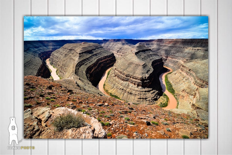 May include: A panoramic view of a winding river snaking through a canyon with layered rock formations. The sky is a mix of blue and white clouds.