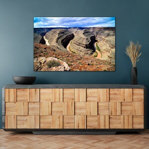 May include: A photograph of a scenic landscape featuring a winding river flowing through a canyon. The canyon walls are a mix of brown, red, and gray rock formations. The sky is blue with white clouds.