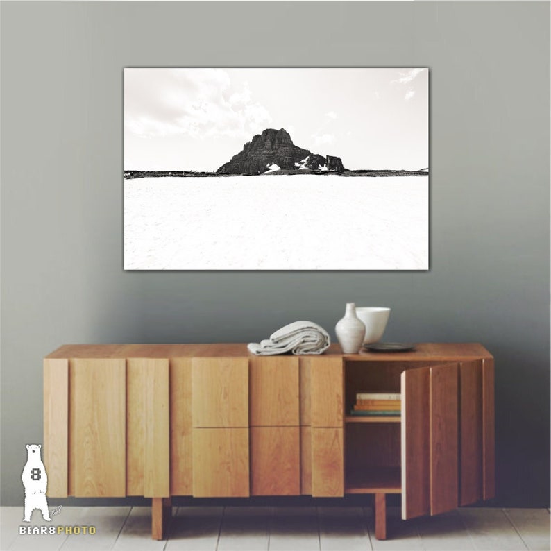 May include: Black and white landscape photograph of a mountain and snow. The artwork is displayed above a wooden cabinet with a modern design. Decorative items, including a vase and bowl, are on top of the cabinet.