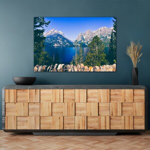 May include: A framed photograph of a mountain lake with snow-capped peaks in the background. The lake is a deep blue color and the mountains are a light blue and white. The photo is hanging on a teal wall above a wooden cabinet.