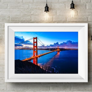 May include: A framed photograph of the Golden Gate Bridge in San Francisco, California. The bridge is lit up at night, with the city lights visible in the distance. The sky is a deep blue with pink and purple clouds.