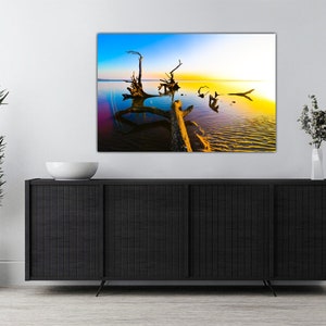 May include: A photograph of a large, weathered tree trunk lying in a body of water. The water is a vibrant blue and green, and the sky is a mix of blue, yellow, and orange. The sun is setting in the distance, casting a warm glow over the scene.