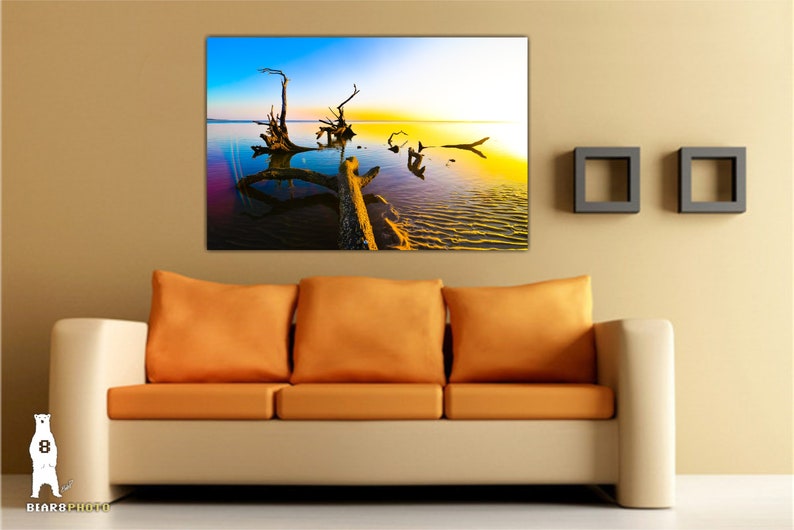May include: A colorful photograph of a large, weathered tree trunk lying in a body of water. The water is a vibrant blue and green, and the sky is a mix of blue, yellow, and orange. The sun is setting in the distance, casting a golden glow over the scene.