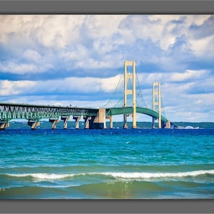 May include: A green and yellow suspension bridge over a body of water with blue water and white capped waves. The bridge is called the Mackinac Bridge.