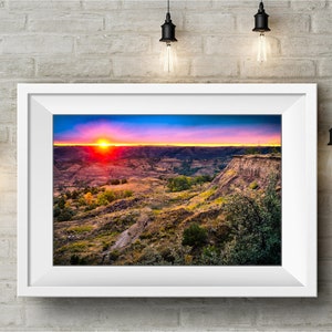 May include: A vibrant sunset over a landscape of rolling hills and canyons. The sky is a mix of pink, orange, and purple, with the sun setting in the distance. The hills are covered in green vegetation and brown rock formations.