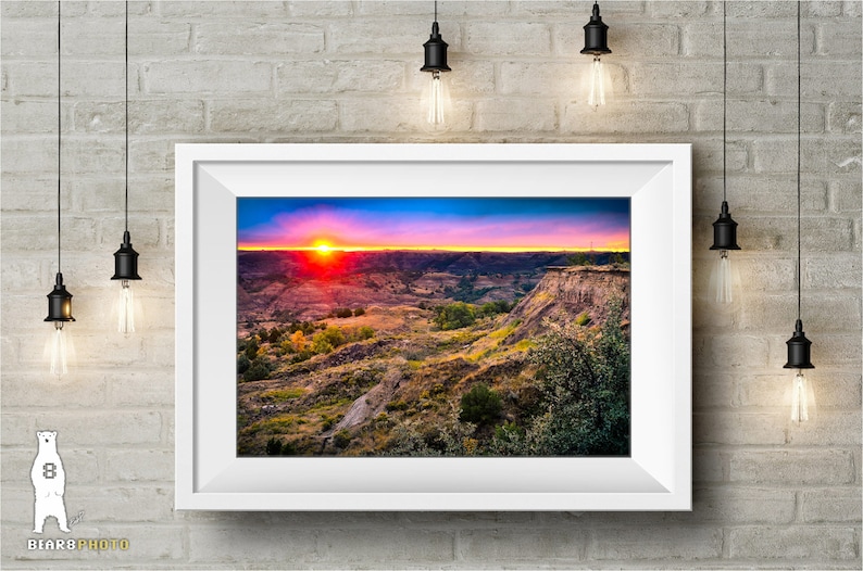May include: A vibrant sunset over a landscape of rolling hills and canyons. The sky is a mix of pink, orange, and purple, with the sun setting in the distance. The hills are covered in green vegetation and brown rock formations.