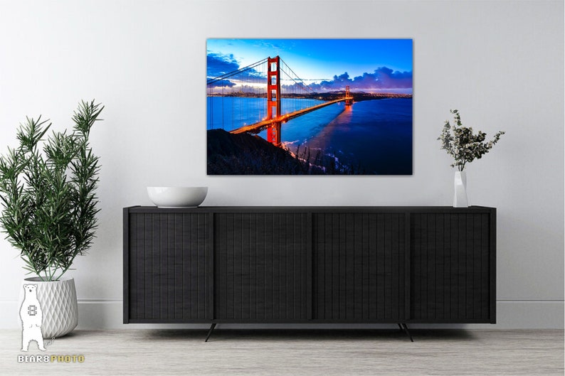 May include: A photograph of the Golden Gate Bridge in San Francisco, California. The bridge is lit up at night, and the water is a deep blue. The sky is a dark blue with clouds.