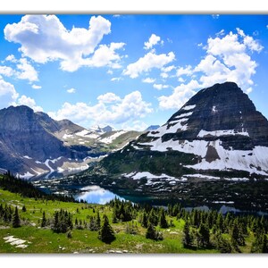 May include: A scenic view of a mountain range with a lake in the foreground. The mountains are covered in snow and the sky is blue with white clouds.