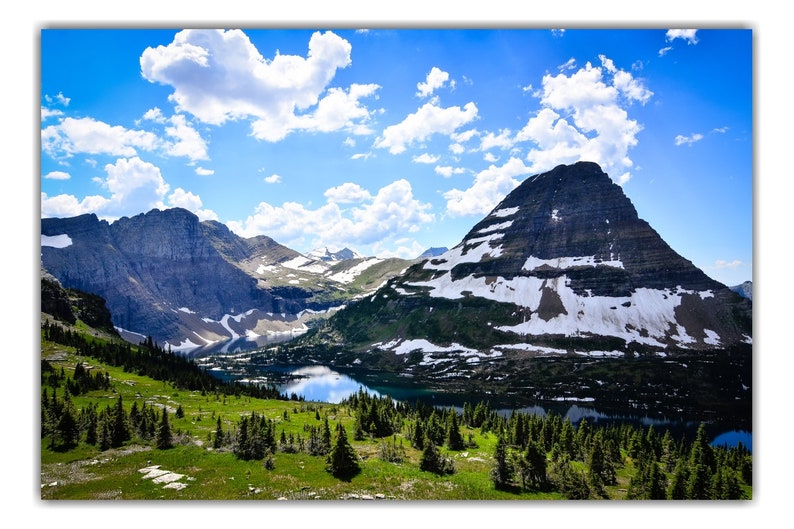 May include: A scenic view of a mountain range with a lake in the foreground. The mountains are covered in snow and the sky is blue with white clouds.