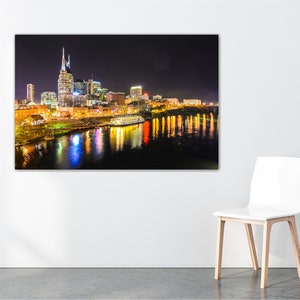 Może przedstawiać: Nocny widok panoramy Nashville z rzeką Cumberland na pierwszym planie. Światła miasta odbijają się w wodzie, tworząc piękny widok.
