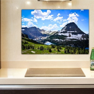 May include: A panoramic view of a mountain range with a lake in the foreground. The mountains are covered in snow and the sky is blue with white clouds.