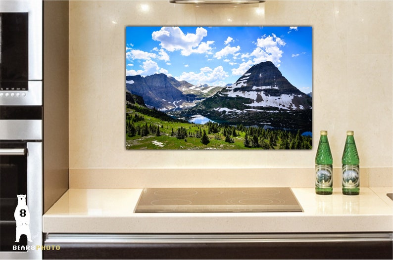 May include: A panoramic view of a mountain range with a lake in the foreground. The mountains are covered in snow and the sky is blue with white clouds.
