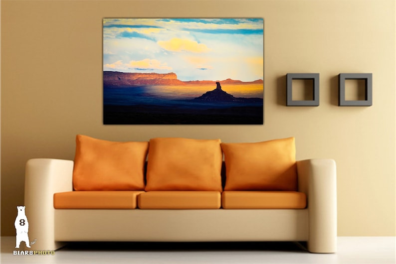 Pode incluir: Uma fotografia de uma paisagem des&eacute;rtica com uma grande forma&ccedil;&atilde;o rochosa em primeiro plano. O c&eacute;u &eacute; de um azul vibrante com nuvens brancas e fofas. As cores s&atilde;o quentes e convidativas, com tons de laranja, amarelo e roxo.
