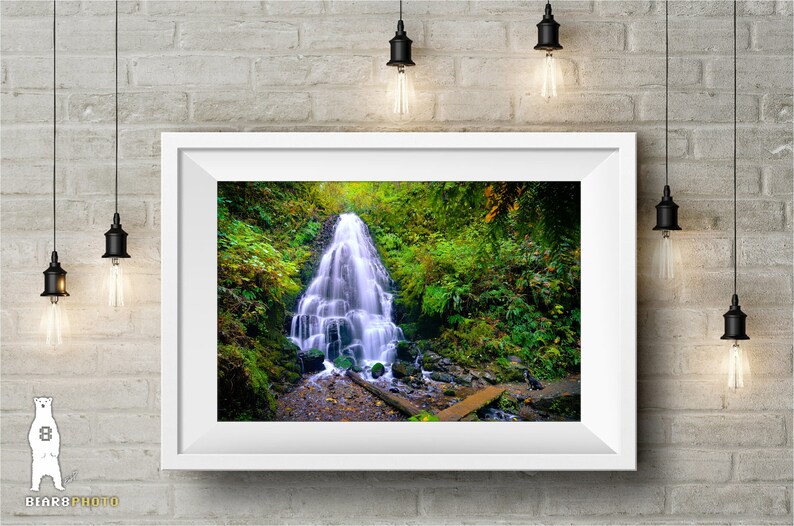 May include: A photograph of a waterfall cascading down a rocky cliff in a lush green forest. The water is flowing over moss-covered rocks and the surrounding foliage is vibrant.