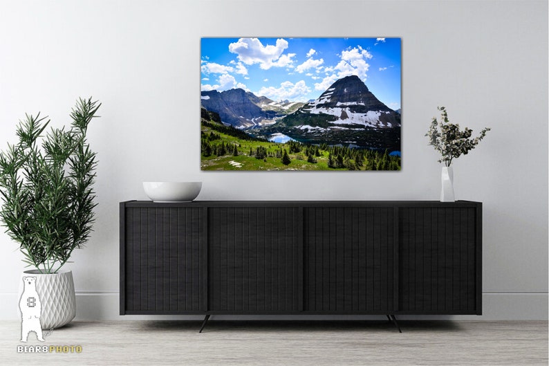 May include: A panoramic view of a mountain range with a lake in the foreground. The mountains are covered in snow and the sky is blue with white clouds.
