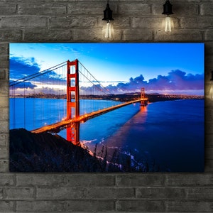 May include: A panoramic view of the Golden Gate Bridge in San Francisco, California. The bridge is lit up at dusk, with the city skyline visible in the background. The water is a deep blue, reflecting the lights of the bridge.