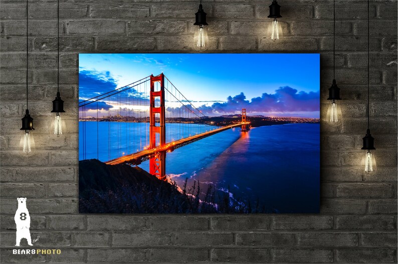 May include: A panoramic view of the Golden Gate Bridge in San Francisco, California. The bridge is lit up at dusk, with the city skyline visible in the background. The water is a deep blue, reflecting the lights of the bridge.