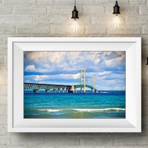 May include: A framed photograph of the Mackinac Bridge in Michigan. The bridge is a suspension bridge with a green and white color scheme. The bridge is over a body of water with blue water and white waves. The sky is blue with white clouds.