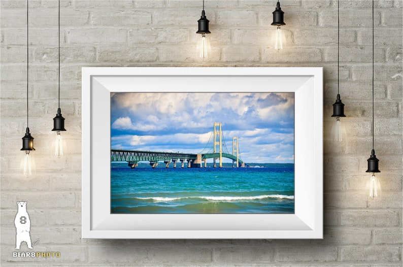 May include: A framed photograph of the Mackinac Bridge in Michigan. The bridge is a suspension bridge with a green and white color scheme. The bridge is over a body of water with blue water and white waves. The sky is blue with white clouds.