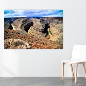 May include: An aerial view of a winding river carving through a canyon in a desert landscape. The river is a light brown color and the canyon walls are a mix of brown, tan, and green.