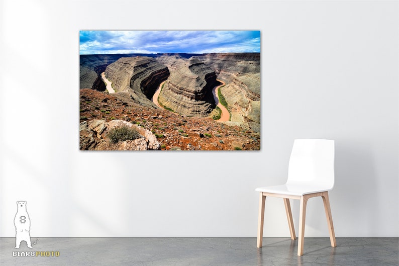 May include: An aerial view of a winding river carving through a canyon in a desert landscape. The river is a light brown color and the canyon walls are a mix of brown, tan, and green.