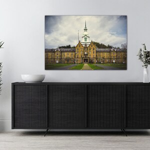 May include: A photograph of an abandoned, yellow brick building with a green roof and a tall tower. The building is surrounded by trees and grass. The sky is cloudy and gray.