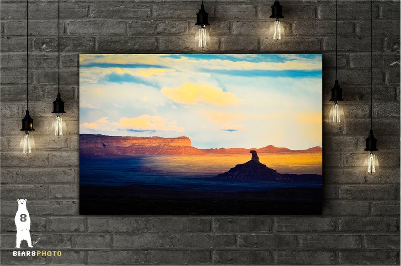 Pode incluir: Uma fotografia panor&acirc;mica de uma cena des&eacute;rtica com uma grande forma&ccedil;&atilde;o rochosa em primeiro plano. O c&eacute;u &eacute; de um azul vibrante com nuvens brancas e fofas. A forma&ccedil;&atilde;o rochosa &eacute; de cor marrom avermelhada e se destaca contra o p&ocirc;r do sol.