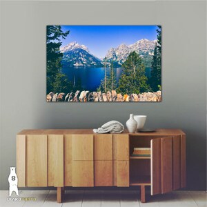 May include: A scenic landscape photograph featuring a mountain range reflected in a blue lake. The mountains are snow-capped and the lake is surrounded by lush green trees.