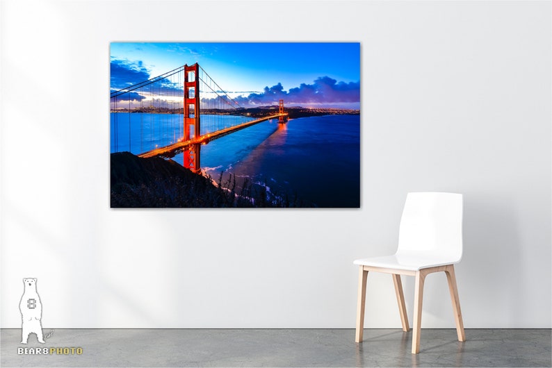May include: A photograph of the Golden Gate Bridge in San Francisco, California. The bridge is lit up at night, and the water is calm and reflective. The sky is a deep blue, and there are clouds in the distance.