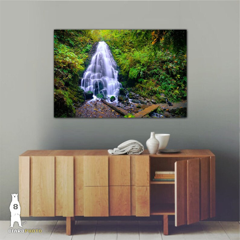 May include: A photograph of a waterfall cascading down a rocky cliffside, surrounded by lush green foliage. The water is clear and white, and the surrounding vegetation is vibrant and healthy.