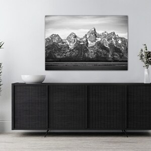 May include: A black and white photograph of a mountain range with snow-capped peaks. The mountains are reflected in a still body of water in the foreground.