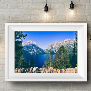 May include: A framed photograph of a scenic mountain lake with snow-capped peaks in the background. The lake is a deep blue color and surrounded by lush green trees. The photo is framed in a white frame.