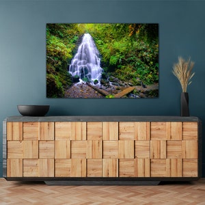 May include: A photograph of a waterfall cascading down a rocky cliff face, surrounded by lush green foliage. The waterfall is in focus, while the surrounding foliage is slightly blurred. The image is taken from a low angle, giving the viewer a sense of the waterfall's height.