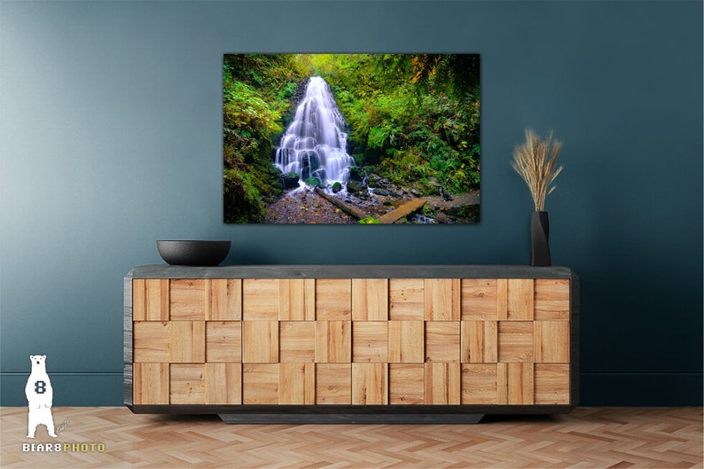 May include: A photograph of a waterfall cascading down a rocky cliff face, surrounded by lush green foliage. The waterfall is in focus, while the surrounding foliage is slightly blurred. The image is taken from a low angle, giving the viewer a sense of the waterfall's height.